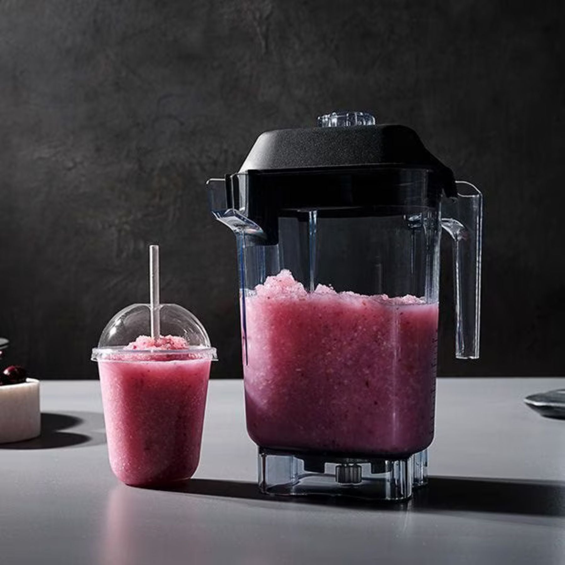 Blender with a pink slushie and a cup on a dark surface