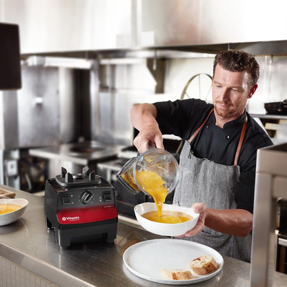Person pouring a blended mixture from a Vitamix Vita-Prep 3 | Blenders Direct into a bowl in a kitchen setting.