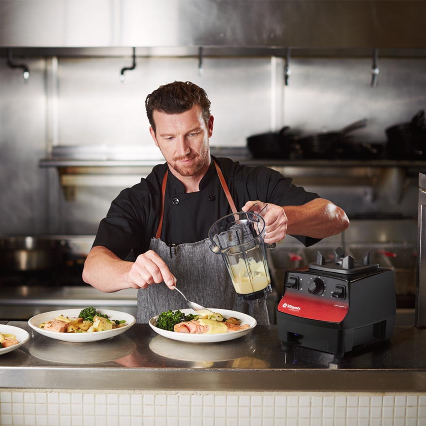 Chef preparing food in a kitchen with a Vitamix Vita-Prep 3 | Blenders Direct and plates of food.