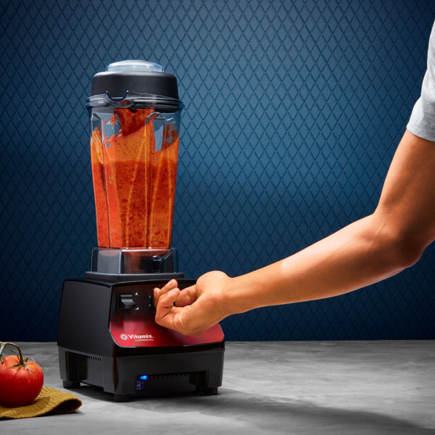 Person using a Vitamix Vita-Prep 3 | Blenders Direct with a red liquid on a blue patterned background