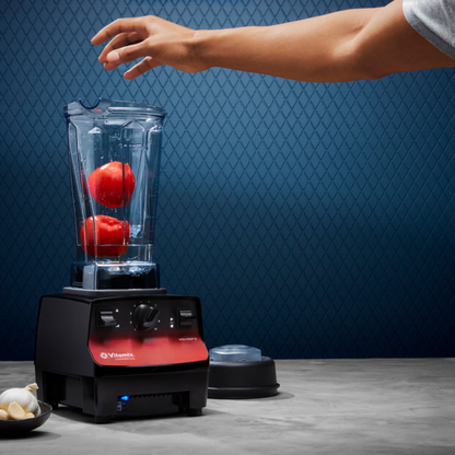 Person preparing to blend tomatoes into a Vitamix Vita-Prep 3 | Blenders Direct with a blue patterned wall in the background.