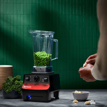 Blender with green ingredients on a kitchen counter against a green tiled wall.