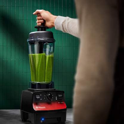 Person using a Vitamix Vita-Prep 3 | Blenders Direct with a green smoothie against a green tiled wall.