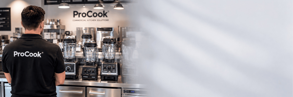 A person wearing a black ProCook t-shirt stands with their back to the camera in a commercial kitchen setting, with multiple Vitamix blenders and other kitchen equipment visible in the background.